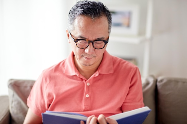 conceito de lazer, literatura e pessoas - homem sentado no sofá e lendo livro em casa