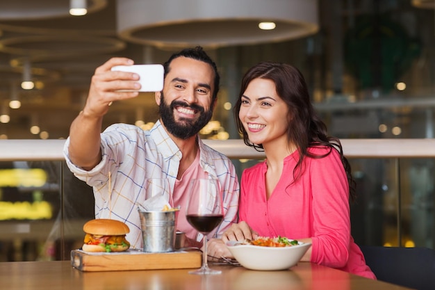 conceito de lazer, tecnologia, encontro, pessoas e feriados - casal feliz jantando e tirando selfie pelo smartphone no restaurante