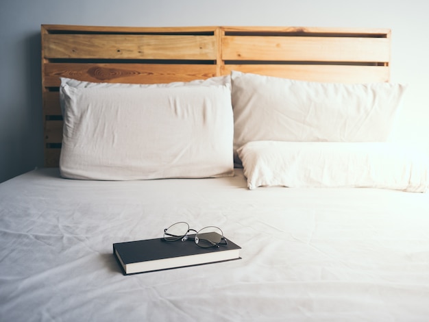 Conceito de ler e relaxar. Monóculos e livro negro na cama de madeira do sótão no quarto.