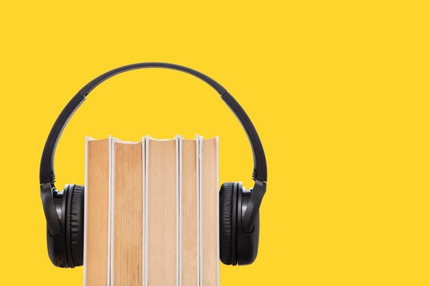 Conceito de livro de áudio Fones de ouvido em livros em fundo amarelo