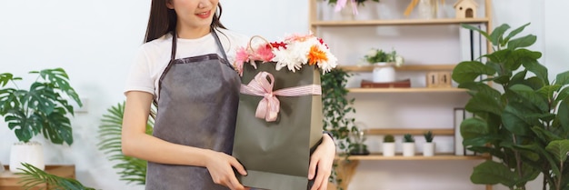Conceito de loja de flores Florista feminina segurando crisântemo e buquê de flores gerbera na sacola de presentes