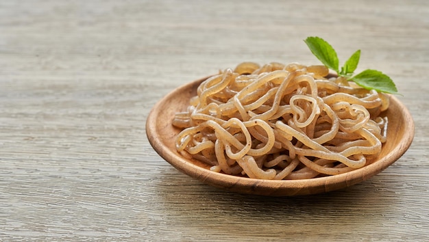 conceito de macarrão konjac de salada marrom e folhas verdes em placa de madeira no fundo da mesa branca