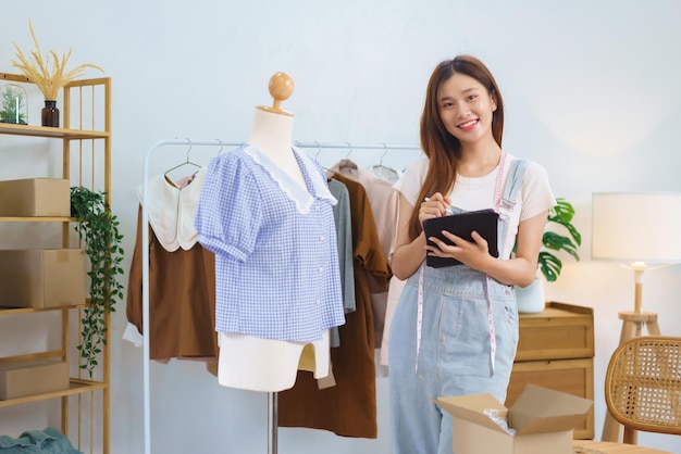 Conceito de marketing online Mulheres asiáticas vendendo roupas em streaming de vídeo e verificando pedidos em tablet