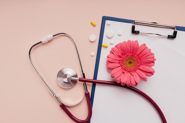 Conceito de medicina Estetoscópio com pílulas e flores em uma mesa rosa