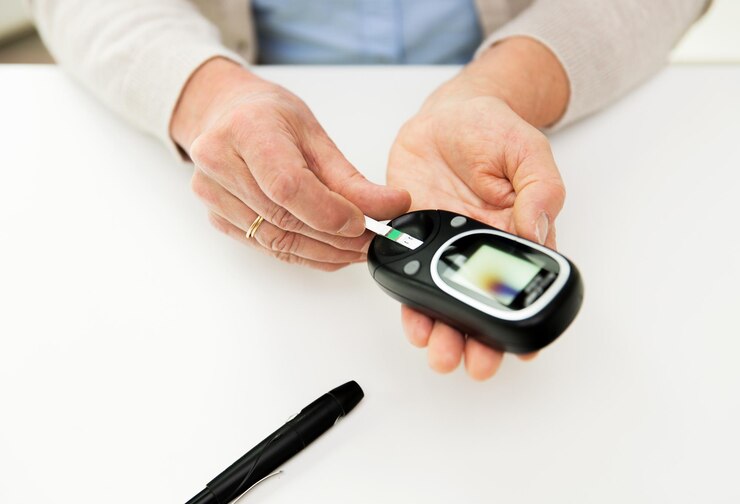 Foto conceito de medicina, idade, diabetes, saúde e pessoas - close-up de uma mulher idosa com glicosímetro e faixa de teste, verificando o nível de açúcar no sangue em casa