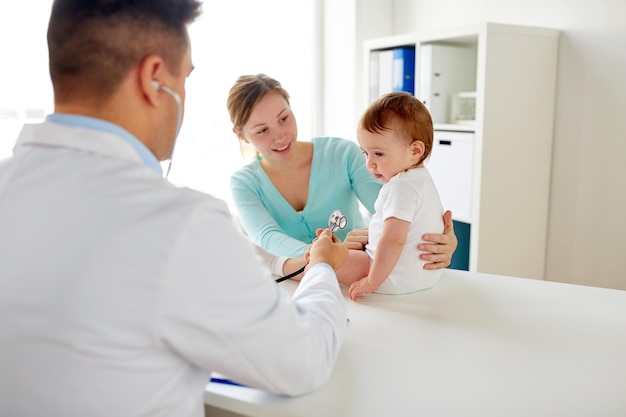 conceito de medicina, saúde, pediatria e pessoas - médico com estetoscópio ouvindo bebê no exame médico na clínica