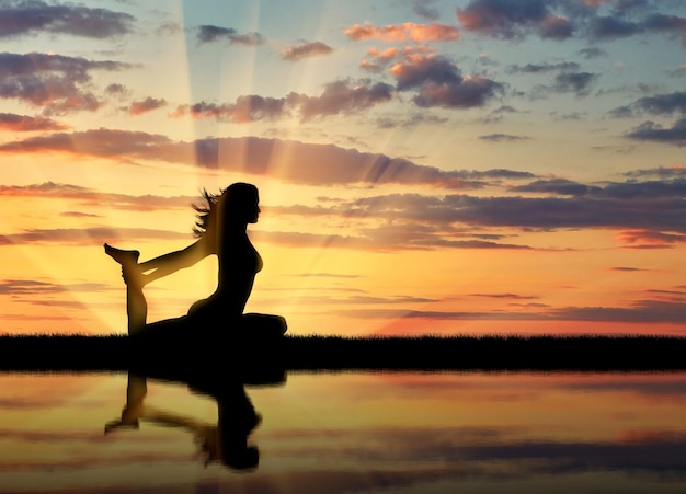Conceito de meditação e relaxamento. Silhueta de uma garota praticando ioga ao pôr do sol e reflexo na água
