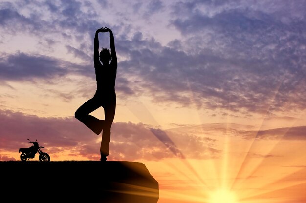 Conceito de meditação e relaxamento. Silhueta de uma menina praticando exercícios de ioga no fundo do sol
