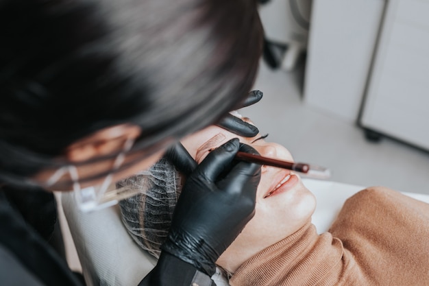 Conceito de microblading de sobrancelhas. Cosmetologista preparando jovem para o procedimento de maquiagem definitiva de sobrancelha.