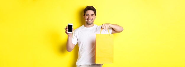 Foto conceito de mobile banking e cashback jovem feliz segurando sacola de compras e mostrando smartphone s