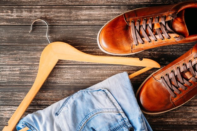 Conceito de moda do homem. Sapatos masculinos de couro casual marrom, jeans e cabide em um fundo escuro