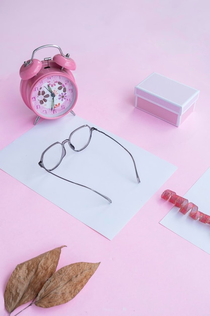 Conceito de moda e beleza deitado com acessórios femininos de óculos quadrados em fundo rosa