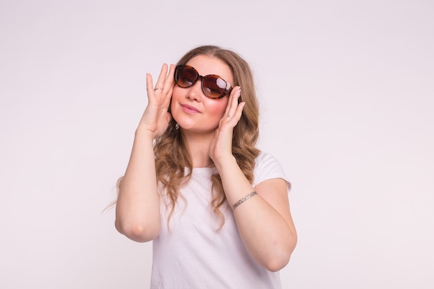 Conceito de moda, estilo e pessoas - mulher jovem e atraente usando óculos escuros sobre a superfície branca