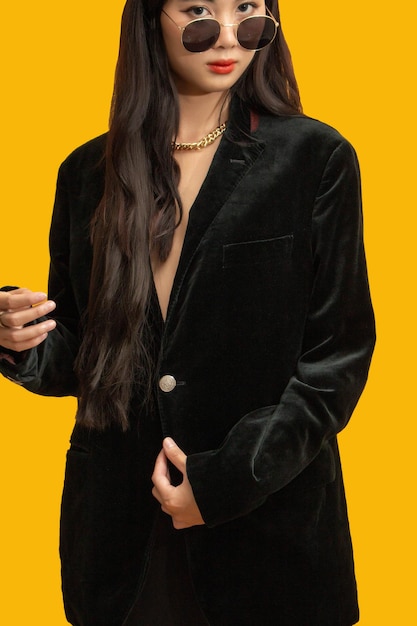 Conceito de moda Mulher na moda usa óculos escuros e casaco de tamanho grande para posar em fundo amarelo