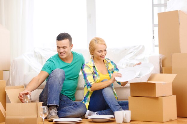 conceito de mudança, casa e casal - casal sorridente desembalando caixas com utensílios de cozinha em nova casa