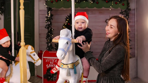 Conceito de Natal dois bebês sentados em cavalos de carrossel dentro de casa e brincando com eles