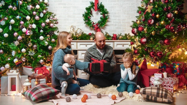 Conceito de Natal feliz família bem sucedida senta-se no cenário de Natal e segurando presentes