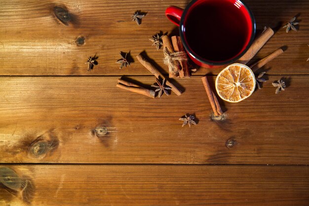 Foto conceito de natal, feriados, culinária e especiarias - close-up da xícara de chá com canela, anis e laranja seca na mesa de madeira de cima