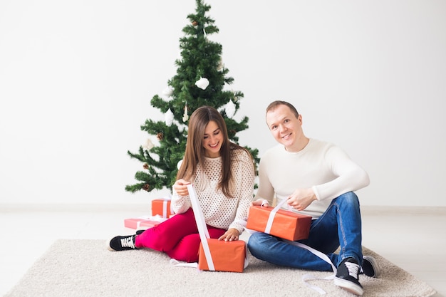 Conceito de Natal, feriados e celebração - jovem bonito e uma bela jovem sentada no tapete e segurando uma caixas de presente.
