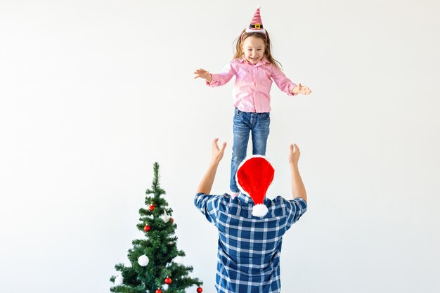 Conceito de natal, feriados e paternidade - pai engraçado com chapéu de papai noel joga sua filha em um fundo branco com espaço de cópia.