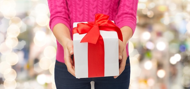 conceito de natal, feriados e pessoas - close-up de mulher de suéter rosa segurando caixa de presente sobre fundo de luzes