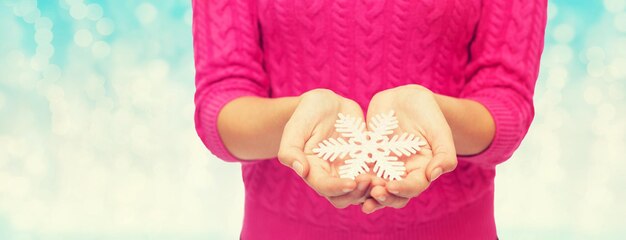 Conceito de natal, feriados e pessoas - close-up de mulher de suéter rosa segurando floco de neve sobre fundo de luzes azuis