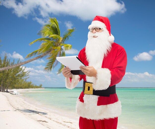 conceito de natal, feriados e pessoas - homem fantasiado de papai noel com bloco de notas sobre fundo de praia tropical