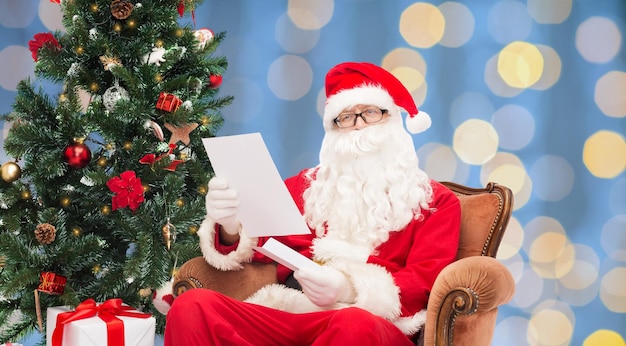 conceito de natal, feriados e pessoas - homem fantasiado de papai noel com carta sobre fundo de luzes azuis