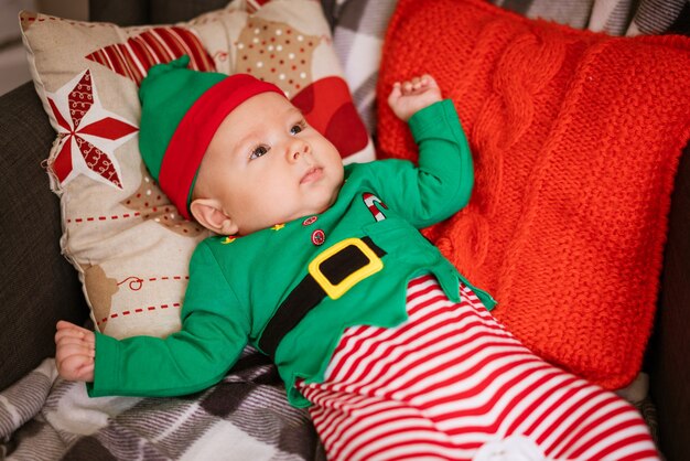 Conceito de Natal garotinho elfo alegre olhando mentiras em almofadas multicoloridas em traje de gnomo s ...