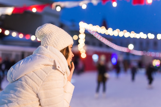 Conceito de Natal, inverno e lazer - jovem feliz perto da pista de patinação no gelo ao ar livre.