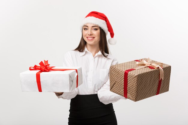 Conceito de natal jovem feliz mulher de negócios caucasiana com chapéu de papai noel dando uma escolha de caixas de presente com espaço de cópia ao lado