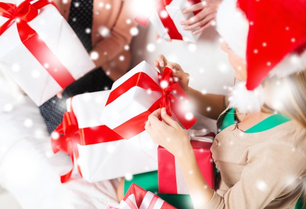 conceito de natal, natal, felicidade, inverno e pessoas - três mulheres com chapéus de ajudante de Papai Noel segurando muitas caixas de presente