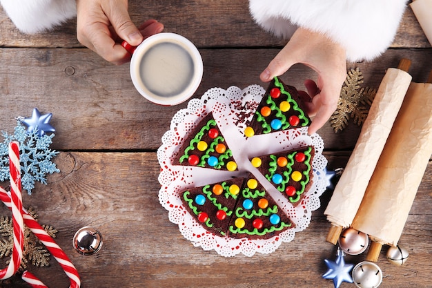 Conceito de Natal. Papai Noel tem uma refeição. As mãos do Papai Noel pegam um pedaço de bolo de chocolate e uma xícara de café, close-up