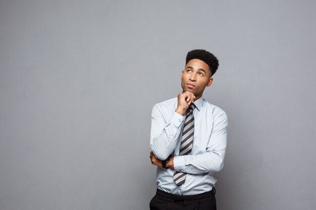 Conceito de negócio - Confiante, jovem e afro-americano, pensativo, segurando a mão no queixo e pensando nos negócios.