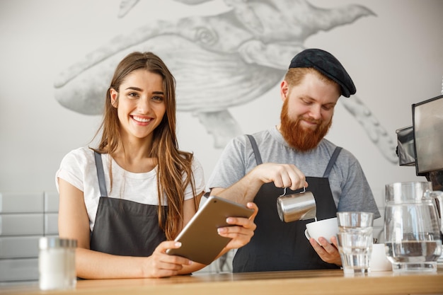 Conceito de negócio de café baristas alegres olhando para seus tablets para pedidos on-line na cafeteria moderna