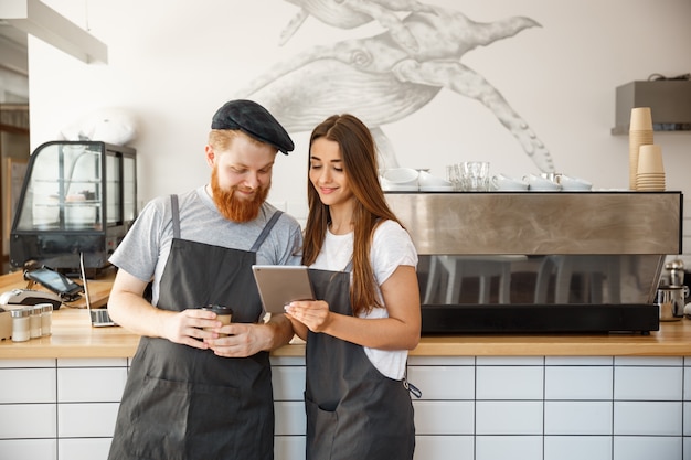 Conceito de negócio de café - baristas alegres que olham seus tablets para pedidos on-line.