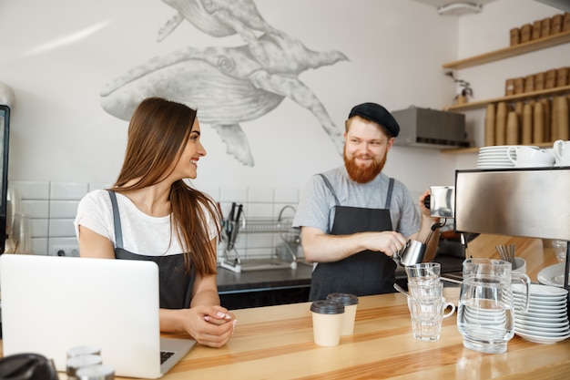 Conceito de negócio de café - Homem barbudo positivo jovem e atraente e atraente casal de barista de senhora desfrutar trabalhando juntos na moderna cafeteria