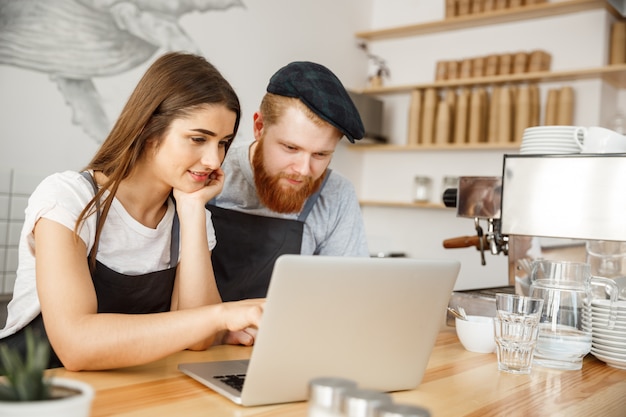 Conceito de negócio de café - satisfeito e os proprietários do sorriso olham no laptop para encomendas on-line na cafeteria