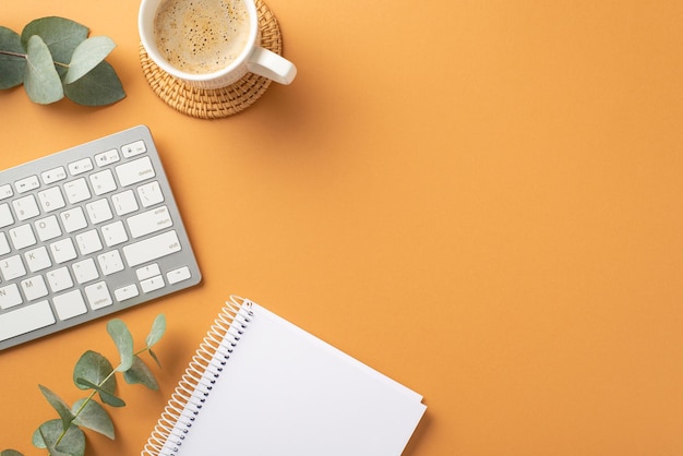 Conceito de negócio Foto de vista superior do caderno de teclado branco da estação de trabalho xícara de café em rattan servindo esteira e eucalipto em fundo laranja isolado com copyspace