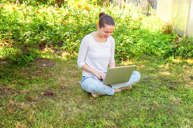 Conceito de negócio freelance. Jovem mulher sentada no gramado verde no parque da cidade trabalhando no computador portátil. Garota de estudante sincera autêntica de estilo de vida estudando ao ar livre. Escritório Móvel