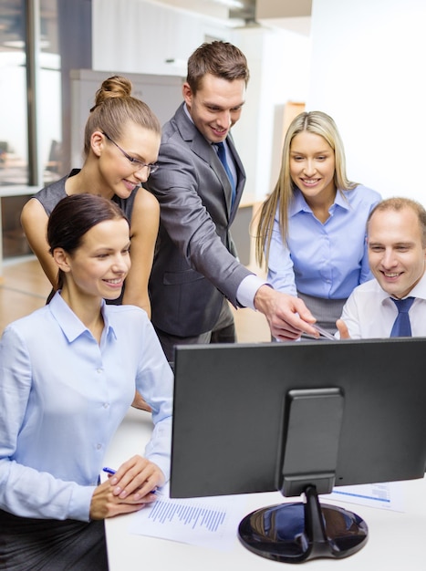 conceito de negócio, tecnologia e escritório - equipe de negócios sorridente com monitor de computador discutindo no escritório