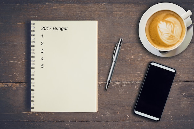 Conceito de negócio - Vista superior do orçamento de escrita do notebook 2017, caneta, xícara de café e telefone na mesa de madeira.