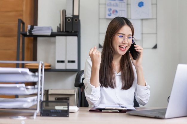 Conceito de negócios A empresária está conversando com o parceiro no smartphone e levantando os braços para comemorar