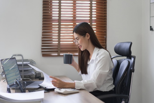 Conceito de negócios A empresária está lendo documentos financeiros e bebendo café no escritório moderno