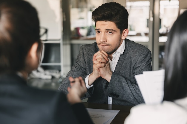 Conceito de negócios, carreira e colocação - homem nervoso e tenso dos anos 30 se preocupando e fechando os punhos durante entrevista de emprego no escritório, com coletivo de especialistas