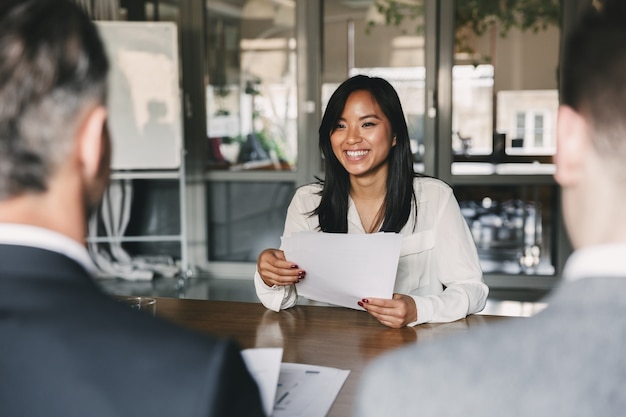 Conceito de negócios, carreira e colocação - jovem mulher asiática sorrindo e segurando o currículo, enquanto está sentada na frente dos diretores durante uma reunião corporativa ou entrevista de emprego