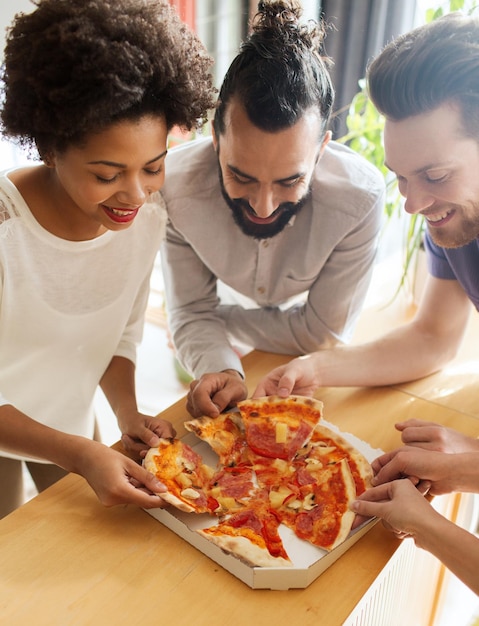 conceito de negócios, comida, almoço e pessoas - equipe de negócios feliz comendo pizza no escritório