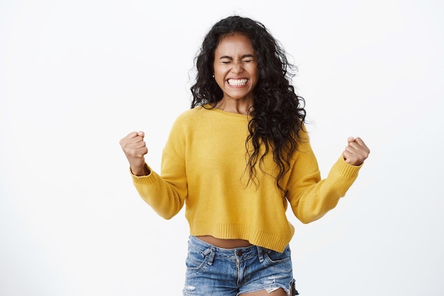 Foto conceito de negócios e bem-estar de confiança bomba de punho de garota afro-americana alegre bem-sucedida e sorrindo diga sim feche os olhos da felicidade celebrando excelentes notícias vencedoras