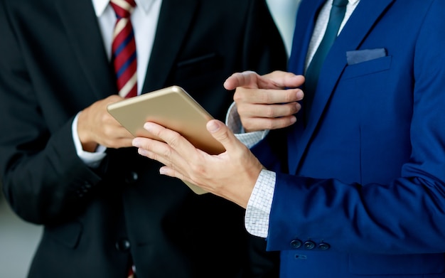 Conceito de negócios e escritório. Casal de homem de negócios vestindo terno azul marinho e terno preto com camisa branca e gravata segurando o tablet ouro e apontando para ele no fundo branco. Isolado