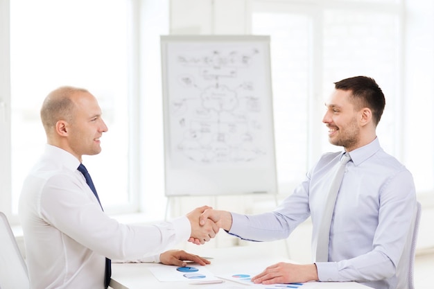 conceito de negócios e escritório - dois empresários sorridentes apertando as mãos no escritório